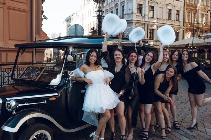 Vecmeitu ballītes grupa pie melna automobiļa