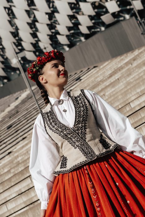 Māsa ar izšūtu vesti un sarkanu vainagu skatās augšup pie Mežaparka estrādes