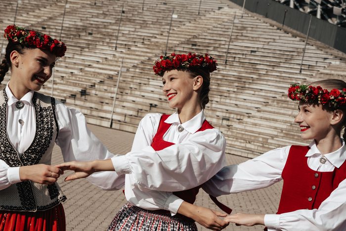 Trīs māsas smejas un turas rokās tautastērpos uz Mežaparka estrādes