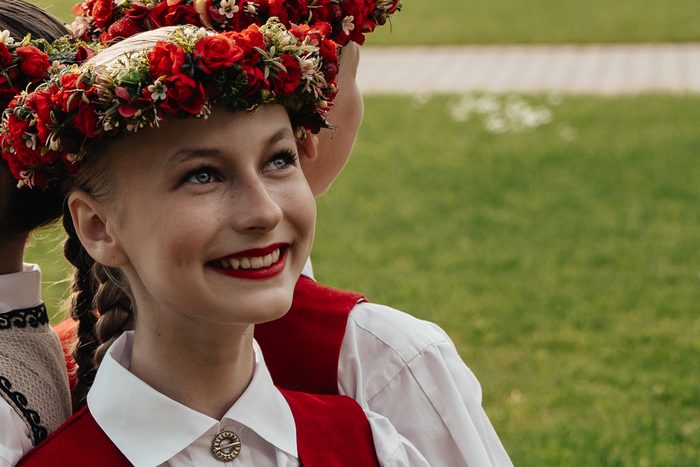 Smaidošas māsas portrets ar sarkanu vainagu un izšūtu vesti Mežaparkā