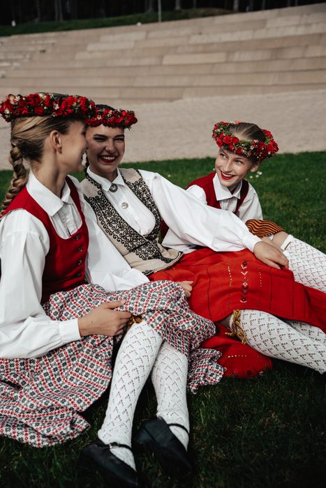 Trīs māsas tautastērpos sēž zālē un smejas pie Mežaparka estrādes