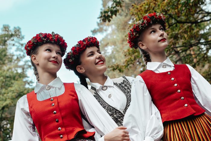 Trīs māsas ar sarkaniem vainagiem skatās augšup zem rudens kokiem Mežaparkā