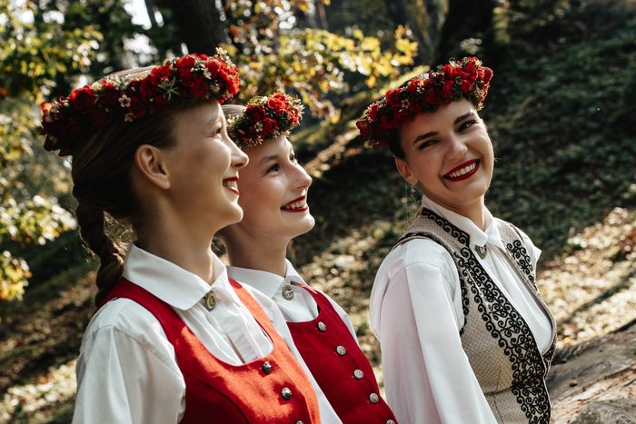 Trīs māsas smejas profilā rudens mežā Mežaparkā tautastērpos