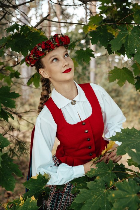 Māsa sarkanā vestē un vainagā starp kļavu lapām rudens Mežaparkā