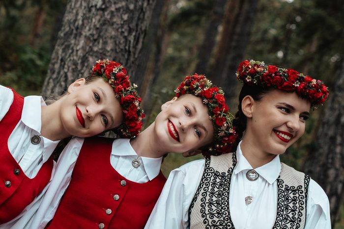 Trīs māsas ar sarkaniem vainagiem smaida, galvas kopā, Mežaparka mežā