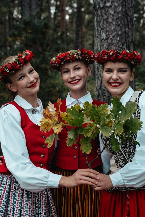 Trīs māsas tautastērpos tur ozola zarus un smaida Mežaparka mežā