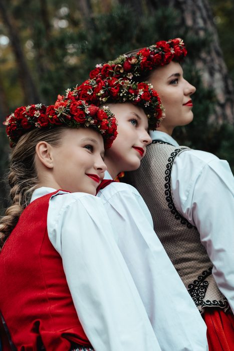 Trīs māsas ar sarkaniem vainagiem skatās sānis Mežaparka priežu mežā