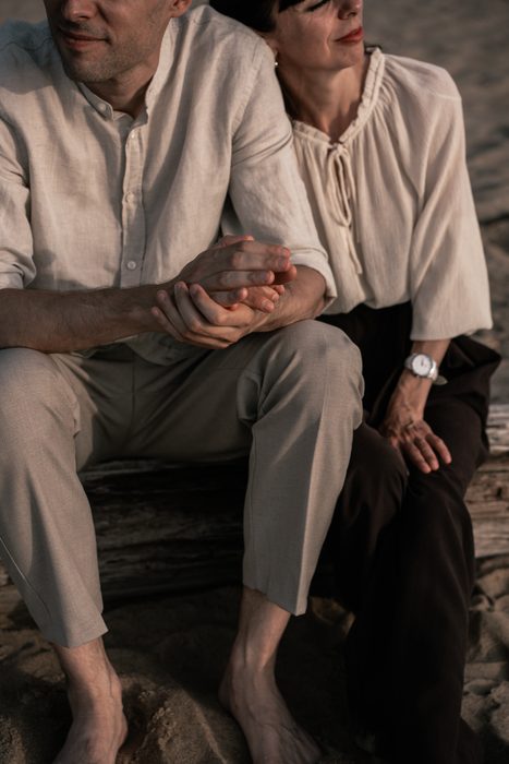 Couple in pale shirts sitting together on the beach
