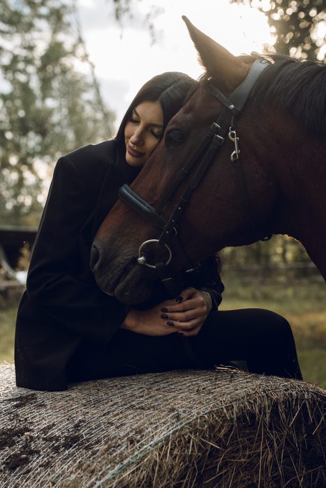 Woman in dark clothing beside a horse outdoors