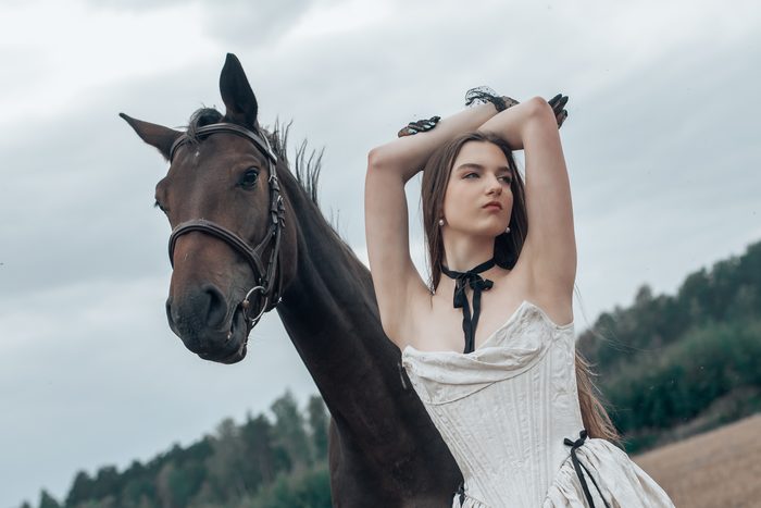 Woman in a pale dress with a black ribbon beside a horse