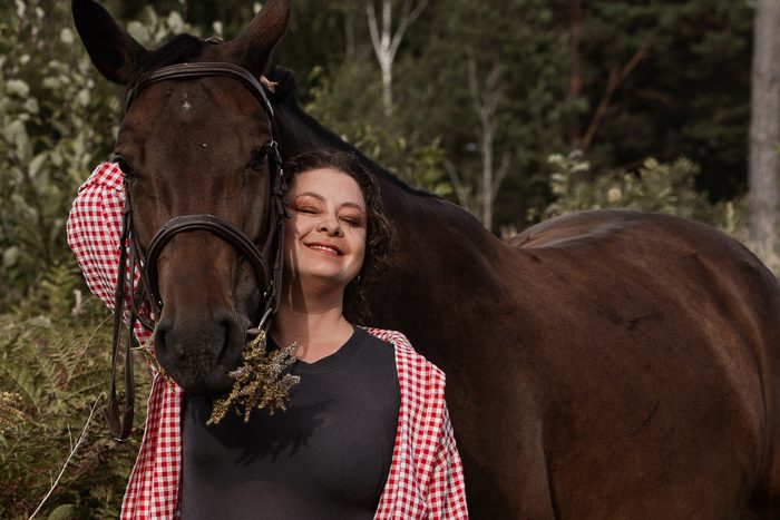 Woman in a pink checked shirt beside a horse