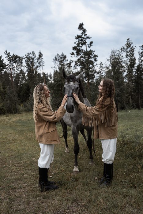 Two women in beige jackets with a grey horse