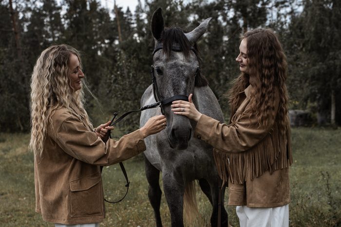 Divas sievietes bēšās jakās ar pelēku zirgu