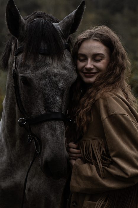 Woman in a beige jacket with a grey horse in a meadow