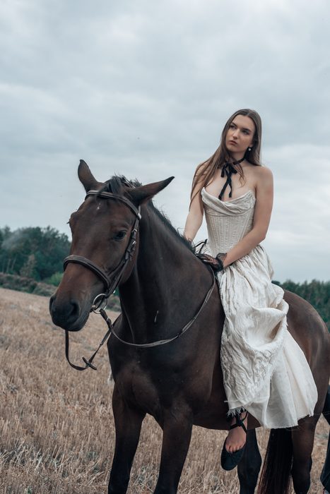 Sieviete gaišā kleitā jāj uz zirga