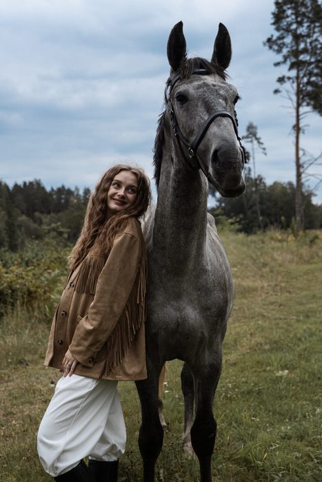 Woman in a beige jacket with a grey horse in a meadow