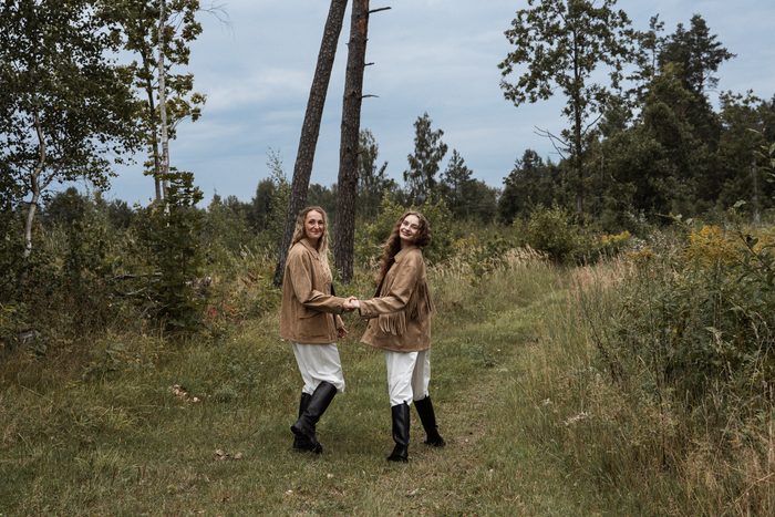 Divas sievietes bēšās jakās sadevušās rokās pļavā