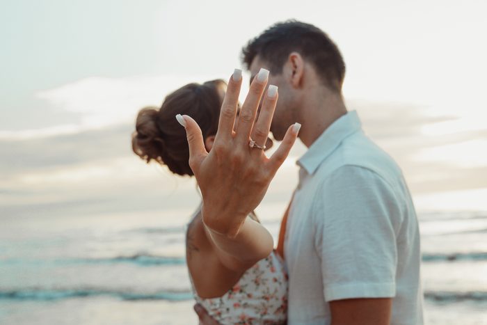 Couple embracing on the beach and showing an engagement ring