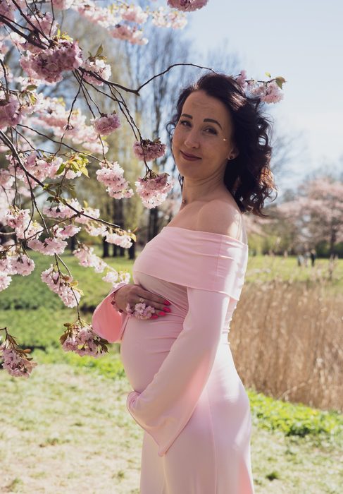 Gaidību portrets rozā kleitā starp ziedošiem zariem