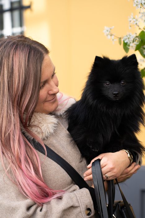 Sieviete tur rokās mazu melnu suni pilsētā