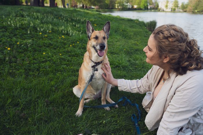 Sieviete gaišā kleitā ar suni un ceriņiem parkā