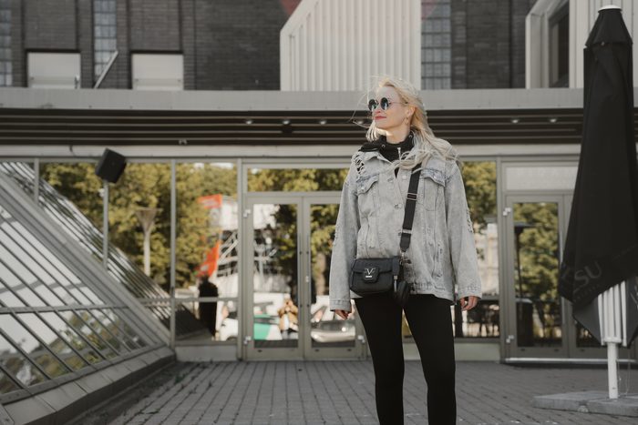 Sieviete džinsa jakā un saulesbrillēs pilsētā