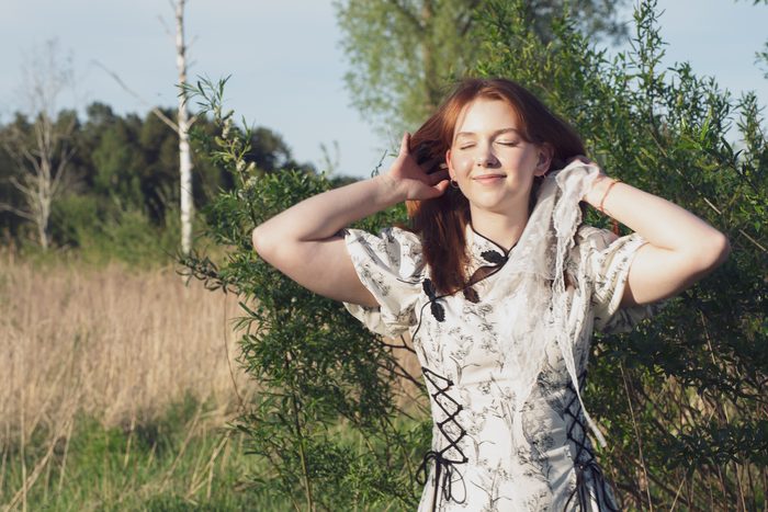 Sieviete rakstainā kleitā saulainā pļavā