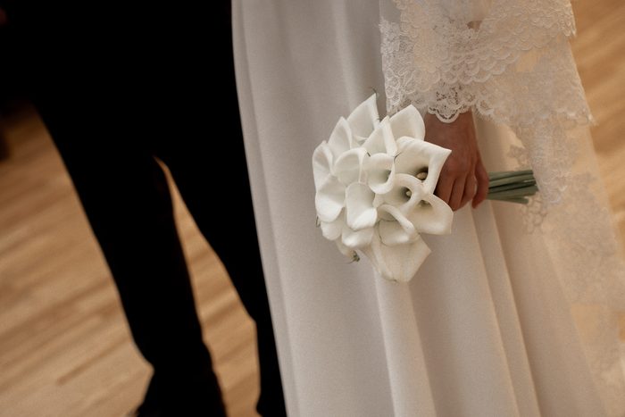 The bride's hand holding a white calla bouquet beside the groom at the ceremony in Jūrmala