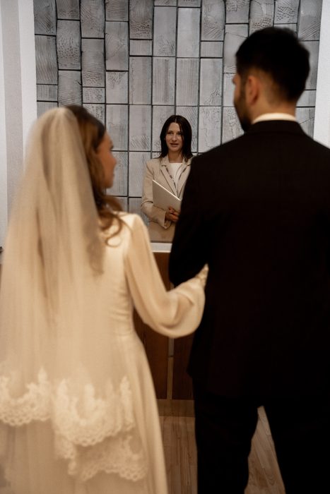 The officiant with a folder and the couple holding hands at the ceremony in Jūrmala