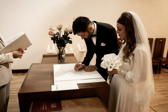 The groom signing the marriage register, the bride with a calla bouquet beside him, in Jūrmala