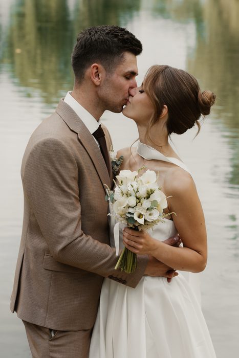 Newlywed portraits with a white bouquet beside the water