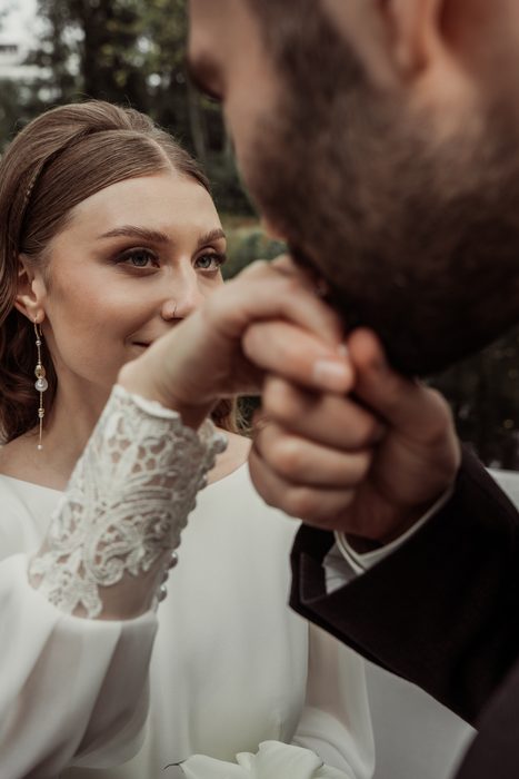 The bride smiling, holding the groom's hand to her face, in Ķemeri Park