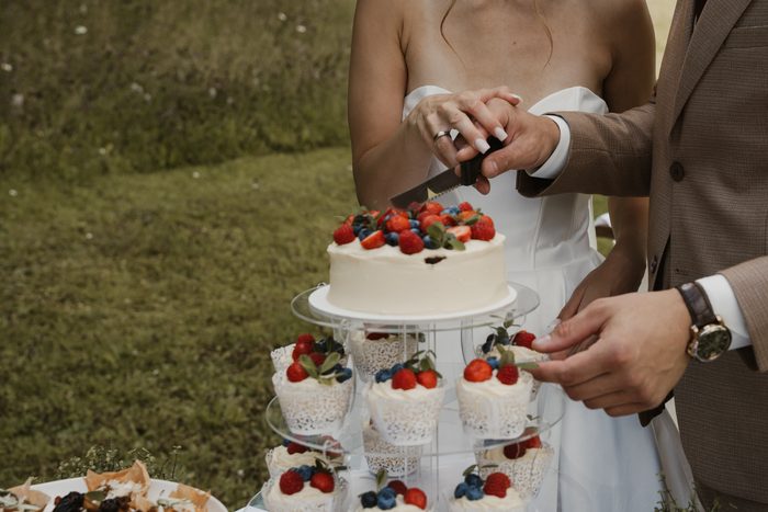 Newlyweds cutting a wedding cake decorated with berries