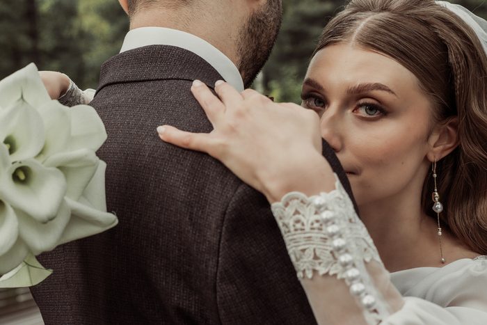 The bride looking over the groom's shoulder, her hand on his jacket, in Ķemeri Park