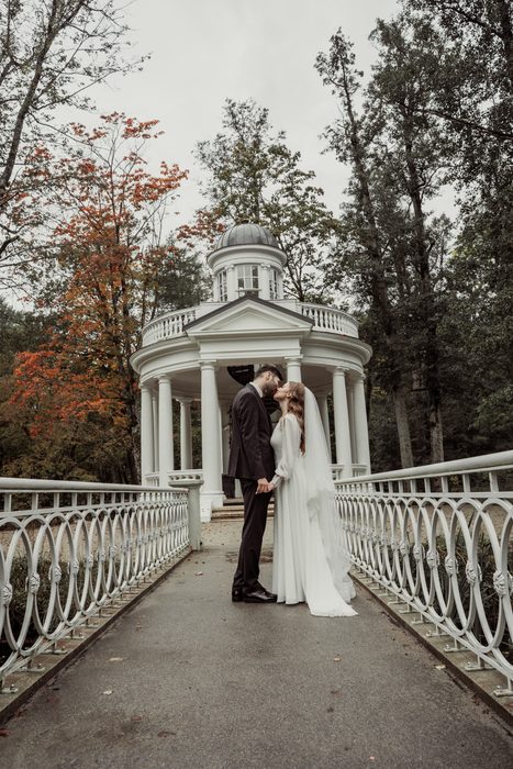 The couple kissing on the bridge by the white rotunda in autumn Ķemeri Park