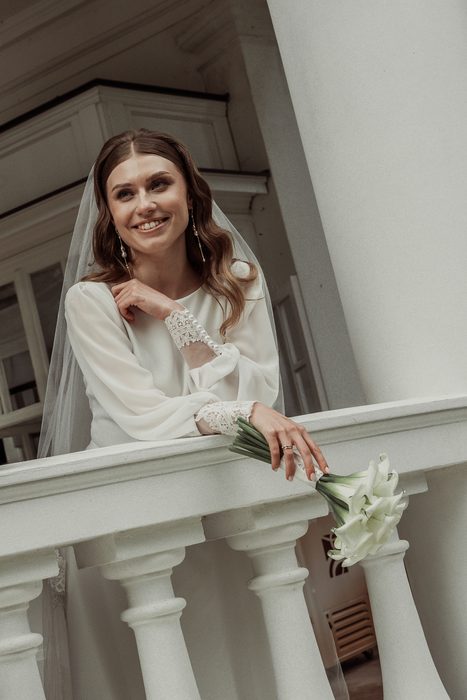 Smiling bride with a calla bouquet at the white rotunda railing in Ķemeri