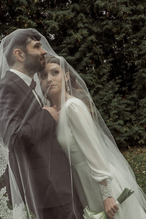 The couple under the veil, the bride's hand on the groom's chest, in Ķemeri Park