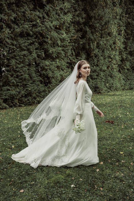 The bride walking across the lawn, veil trailing, in Ķemeri Park