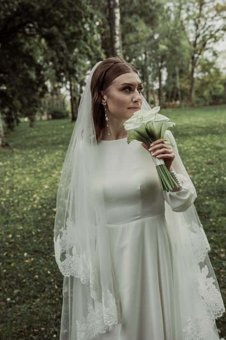 The bride holding a calla bouquet near her face on the lawn in Ķemeri Park