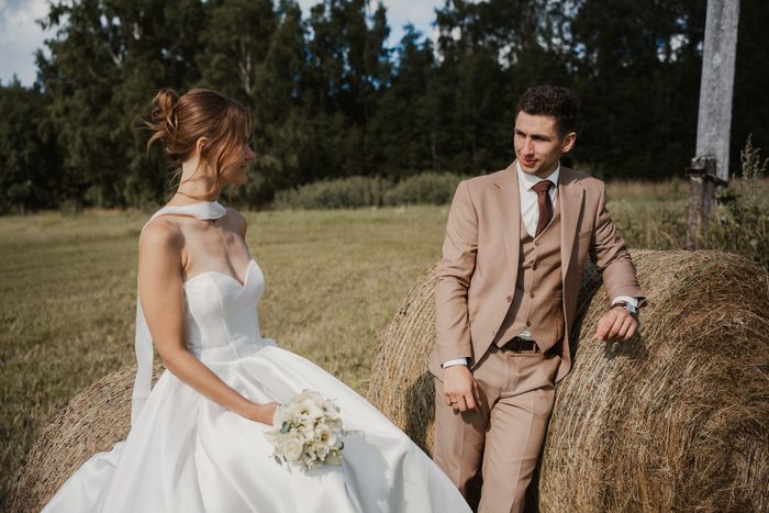 Newlyweds’ photoshoot in a field beside hay bales