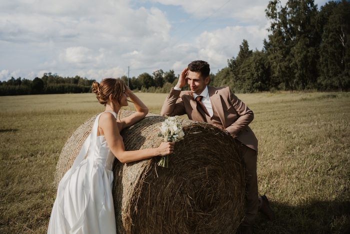 Newlyweds’ photoshoot in a field beside hay bales