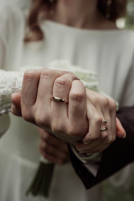 Clasped hands with wedding rings and a calla bouquet in Ķemeri