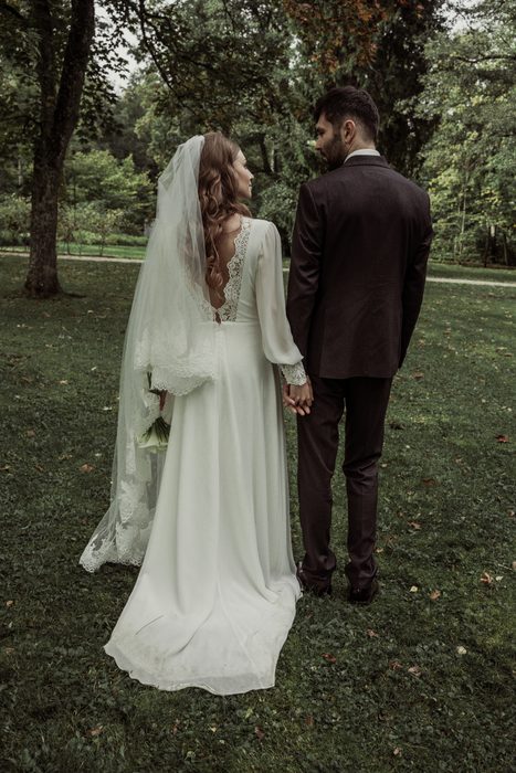 The couple from behind, holding hands, the lace back of the dress visible, in Ķemeri
