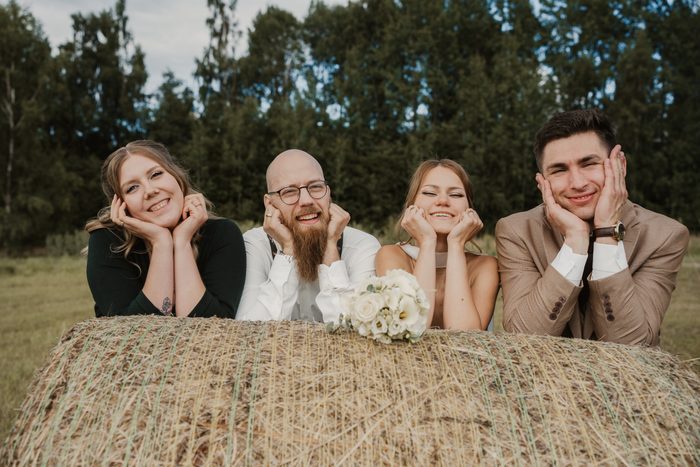 Newlyweds and friends beside a hay bale