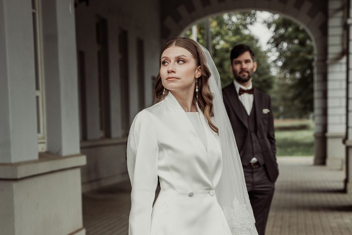 The bride in the colonnade, the groom under the arch behind her, in Ķemeri