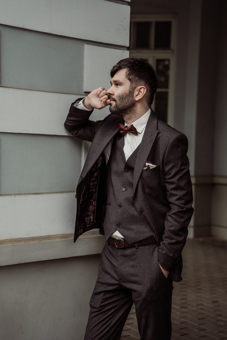 The groom leaning against the building facade in Ķemeri