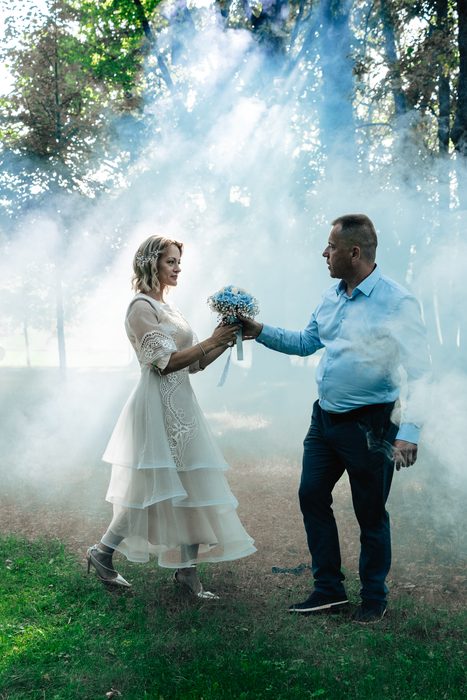 Wedding couple surrounded by blue smoke among trees